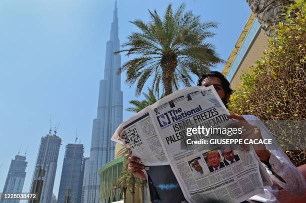 Man reads a copy of UAE-based The National newspaper near the Burj Khalifa, the tallest structure and building in the world since 2009, in the gulf...