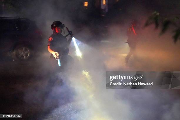 Portland police officer carries a can of pepper spray through smoke during a crowd dispersal on August 14, 2020 in Portland, Oregon. The Portland...