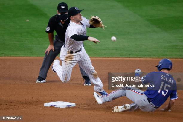 Trevor Story of the Colorado Rockies throws to first base to complete the double play as Nick Solak of the Texas Rangers slides in and umpire Rob...