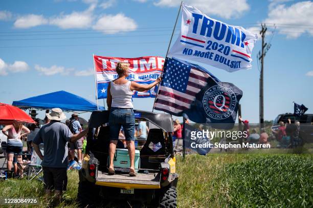 Woman holds a Trump 2020 flag and a Q Anon flag outside of Mankato Regional Airport as President Donald Trump makes a campaign stop on August 17,...