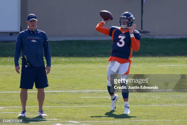 Quarterback Drew Lock of the Denver Broncos throws a pass on the field as Offensive Coordinator Pat Shurmur looks on during a training session at...