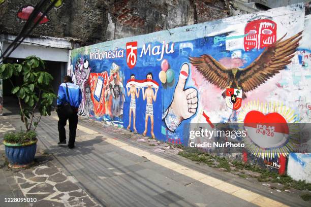 Man walks passing the Independence Day theme mural painted by Bambang and his friends on the street wall near the Bambang's street paint studio...