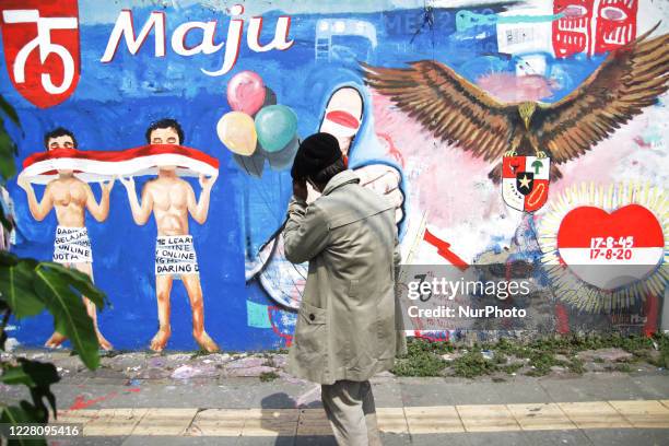 Bambang stands in front of the Independence theme mural painted by him and friends on the street wall next to his street paint studio during the...
