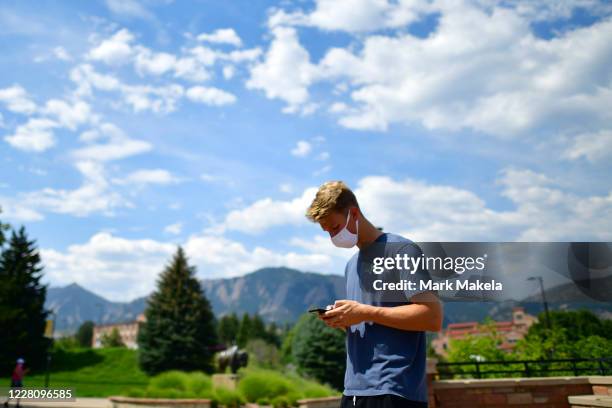 An incoming freshman wears a face mask and uses his smartphone after registering upon arriving on campus at University of Colorado Boulder on August...
