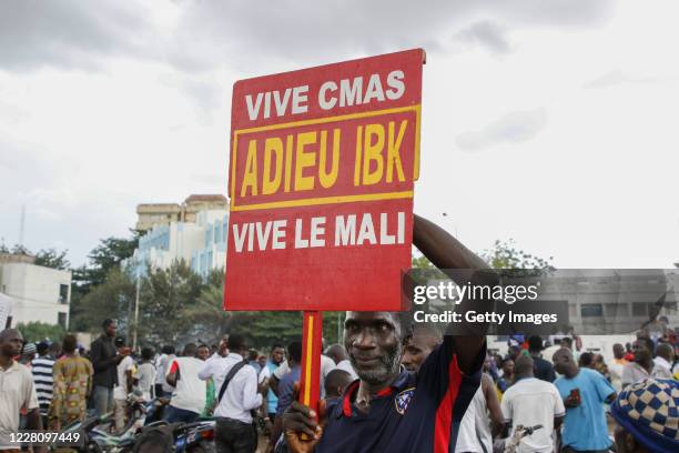 Man holds a sign saying goodbye to IBK, referring to Malian President Ibrahim Boubacar Keita, as soldiers parade in vehicles along the Boulevard de...