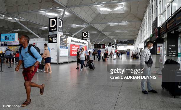 Travellers, some wearing a face mask or covering due to the COVID-19 pandemic, walk through the terminal building at London Stansted Airport,...