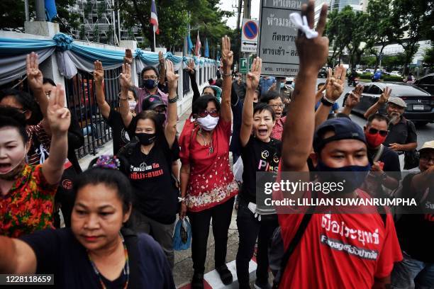 Anti-government protesters hold up three-finger salutes as they wait for detained activists to leave on bail outside the Criminal Court in Bangkok on...