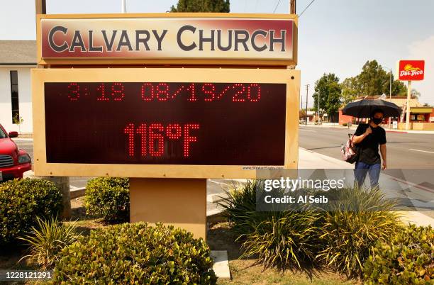 Leo Dumayag with umbrella for shade walks past the thermometer at Calvary Church in Woodland Hills as it registers 116 degrees Fahrenheit Wednesday...