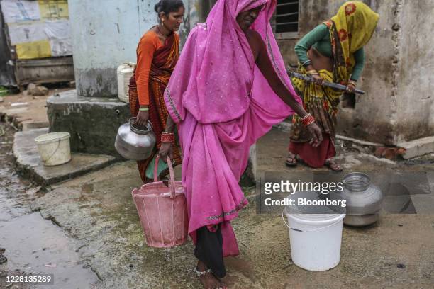 Woman carries a bucket of water as others use a community hand pump at a village in Tikamgarh district, Madhya Pradesh, India, on Friday, Aug. 7,...
