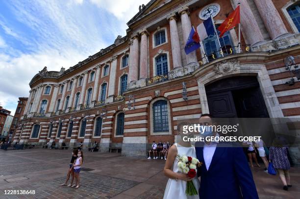 Couple poses wearing face maks for wedding photos in front of the city hall, at the Capitole square, in Toulouse southern France, on August 21, 2020....