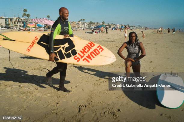 From left: Nathan Fluellen and Joi K. Madison warm up before surfing a 1ft swell at El Porto Beach Tuesday, Aug. 11, 2020 in Manhattan Beach, CA....