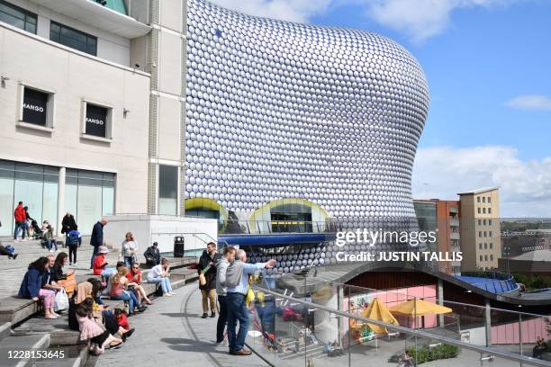 People sit outside the Bullring shopping centre in Birmingham, central England on August 22 as Britain's second-city, home to more than one million...