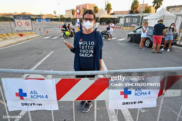 Holidaymaker wearing a face mask and a jersey reading "I drop everything and live in a boat", and returning from Sardinia by ferry waits outside her...