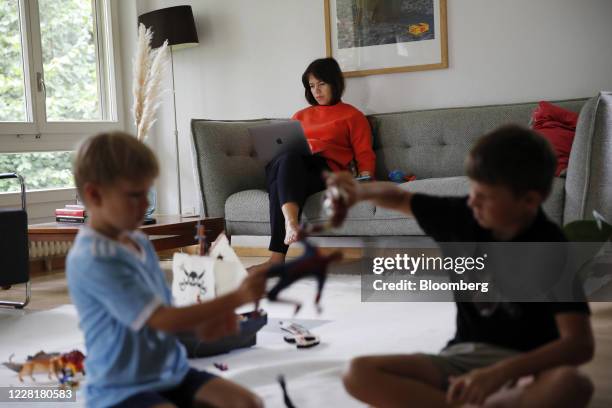 Woman works at an Apple Inc. Laptop computer on the couch as children play with toys on the floor in this arranged photograph taken in Bern,...