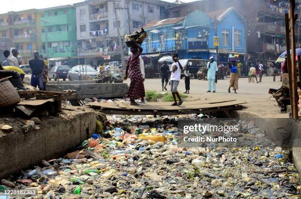 People walk past a drainage channel blocked with bottles and disposable foam food take away containers along Adeniji Adele on Lagos-Island in Lagos,...