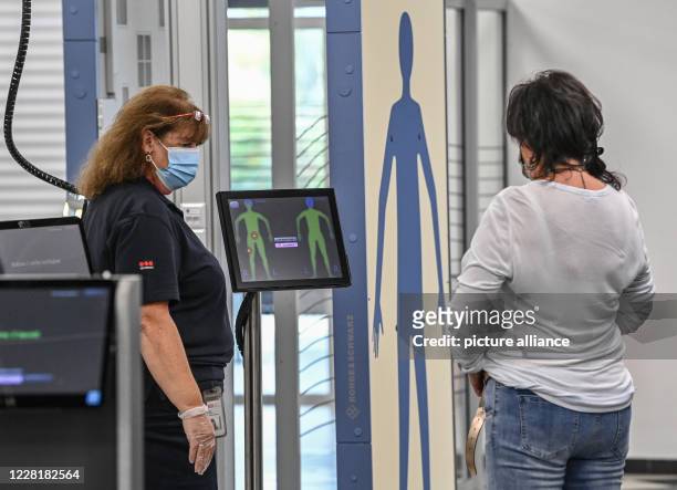 August 2020, Brandenburg, Schönefeld: A traveler is checked at the body scanner by a member of the security control staff in the building of Terminal...