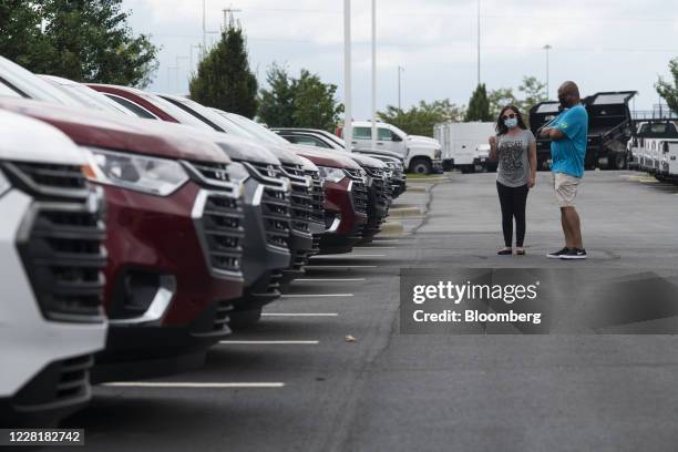 Salesperson and customer wear protective masks while viewing General Motors Co. Chevrolet vehicles displayed for sale at a car dealership in Grove...