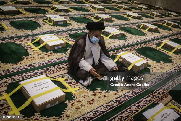 Sheik Sayed Musavi wearing a protective mask prays among cardboard boxes and yellow ribbons to mark the distances between the faithful at the Mosque...