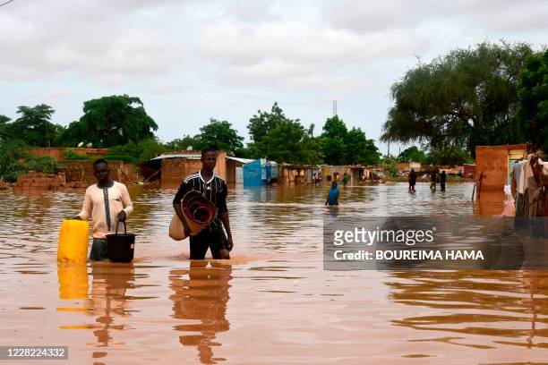 People carry their belongings while walking in a street flooded by the waters from the Niger river that flooded in the Kirkissoye neighbourhood in...