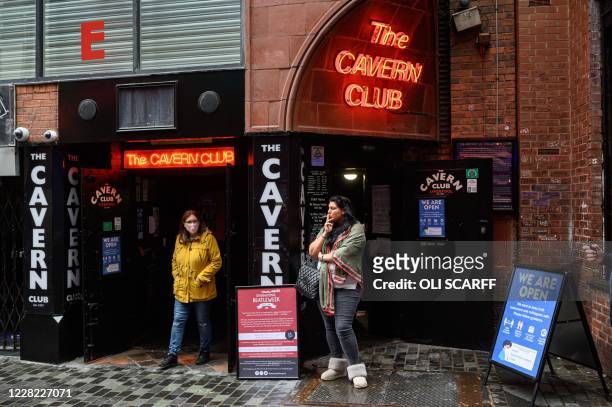 Woman smokes under the neon sign for the Cavern Club as it reopens to the public with live music to host their annual 'Beatleweek' celebration of...