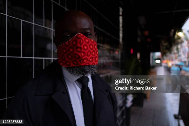 On a rainy night in Soho, security man 'H' wears a bright red facial covering outside a business at a time when recently re-opened bars and...