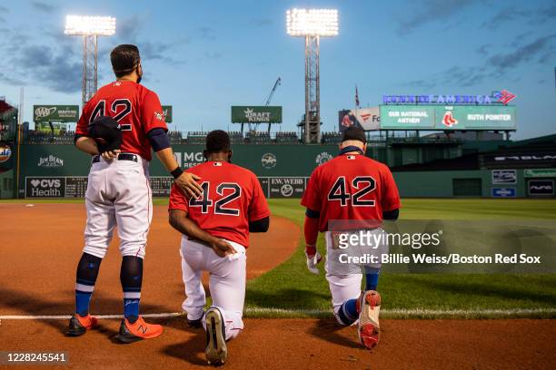 Alex Verdugo and Jackie Bradley Jr. #19 of the Boston Red Sox kneel alongside Michael Chavis during the National Anthem during a pre-game ceremony in...