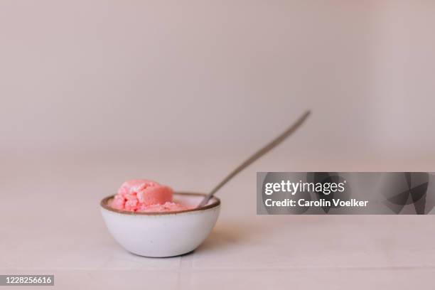 small white ceramic bowl with a spoon and strawberry ice cream on a cream colored surface - ice cream bowl side view stock pictures, royalty-free photos & images