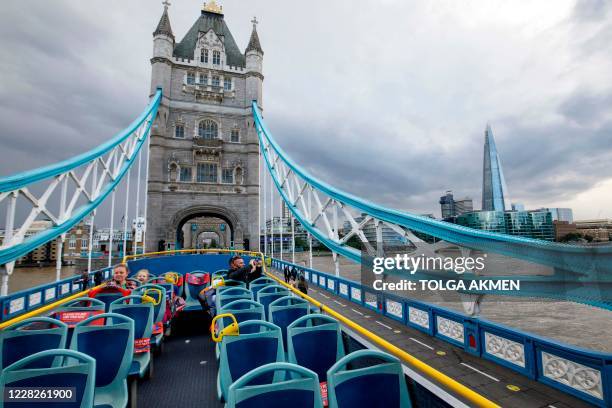 Man takes pictures on Tower Bridge from the near empty top of an open top tourist tour bus in central London on August 24, 2020. - The World Travel &...