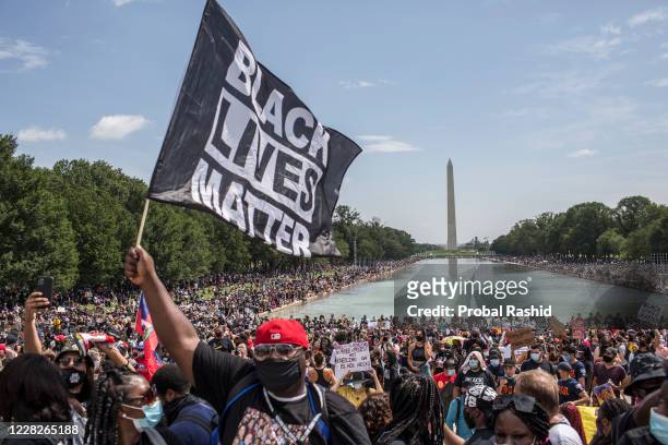 Demonstrator holding a flag with Black Lives Matter written on it while attending the "Commitment March: Get Your Knee Off Our Necks" protest against...