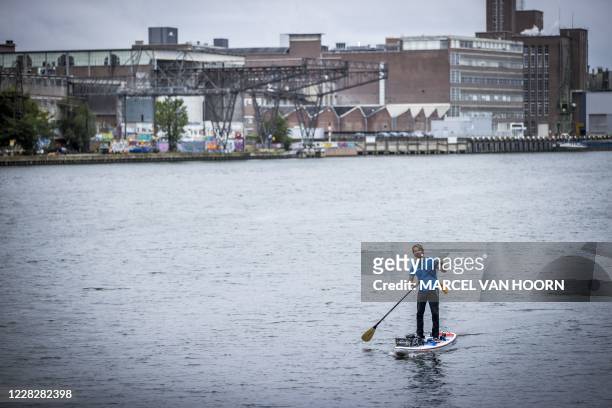 Merijn Tinga stands on a paddle board at the start of the Plastic Soup Surfer expedition in Maastricht on August 31, 2020. - In 16 days, Tinga will...