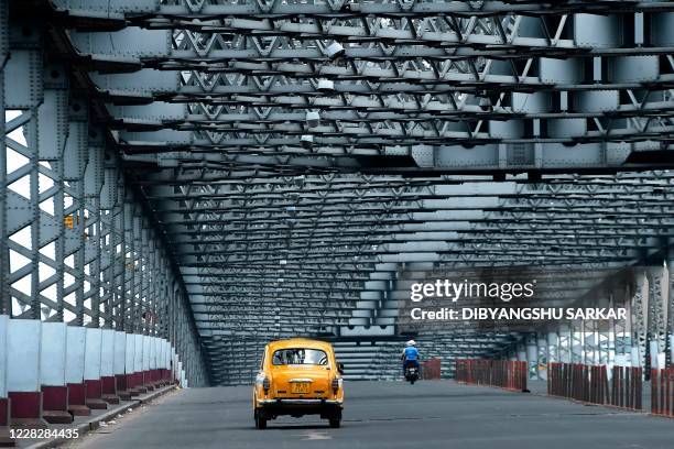 Taxi drives past the deserted Howrah Bridge during a day long state-imposed lockdown as a preventive measure against the surge Covid-19 coronavirus...