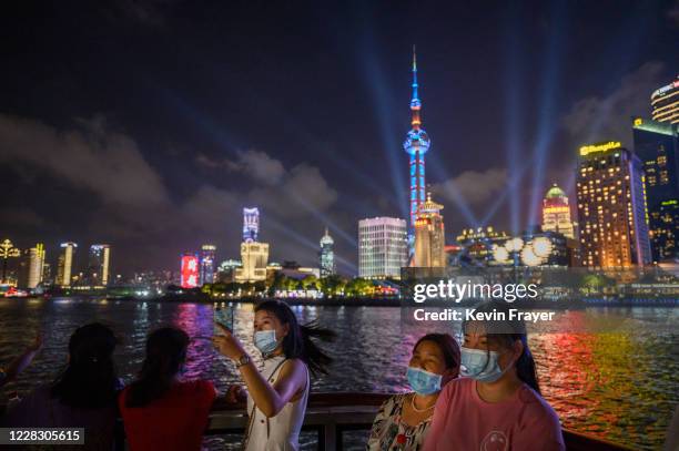 Chinese tourists, wear protective masks as they stand on the deck of a tourist boat on the Huangpu River as the skyline of the Pudong district can be...