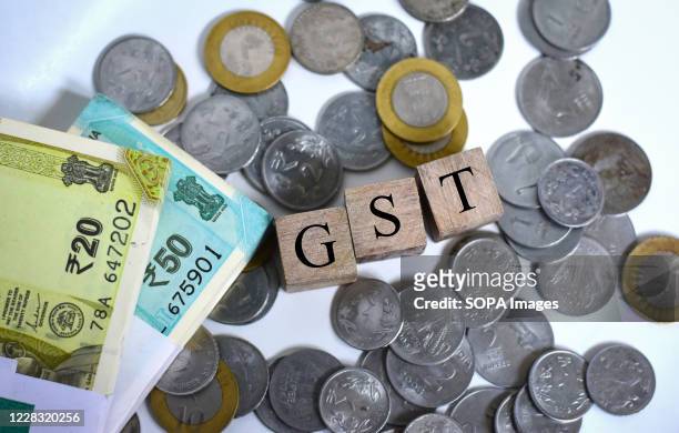 In this photo illustration Indian currency coins and fifty, twenty rupees notes are seen with a GST cube blocks.