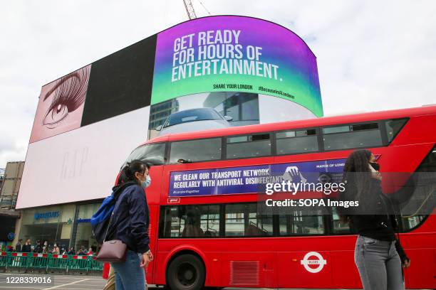 Women wearing face masks walk past a London double decker bus which has a 'We clean our transport network regularly with antiviral disinfectant'...