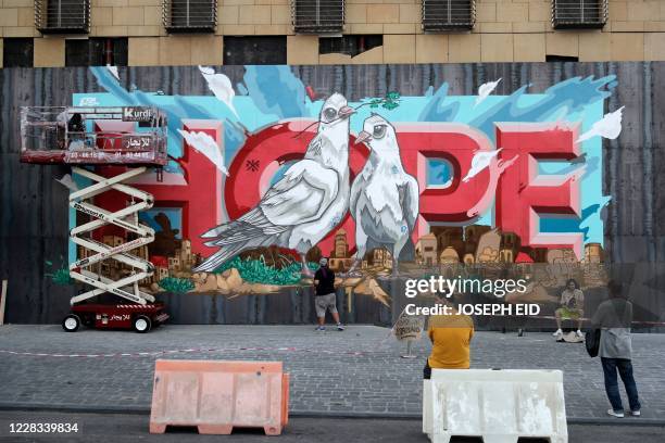 Onlookers watch as artists from the group REK paint a mural on a barrier erected in front of Le Grey hotel in Beirut's downtown district, depicting...