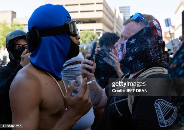 Counter-protester blows cigarette smoke in the face of a patriot militia member as he marches in support of local police officers in front of the...