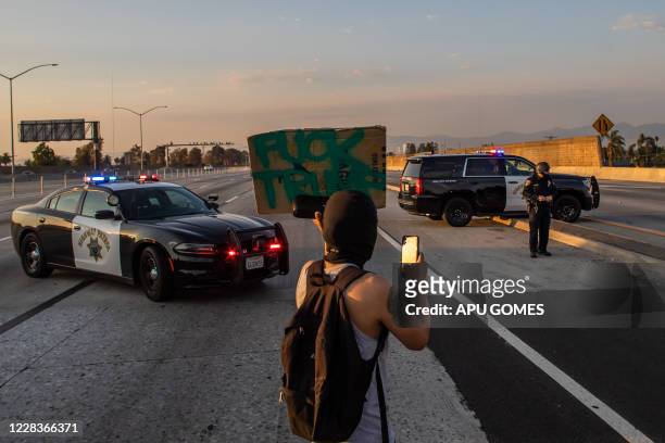 Man holds a sign in front of Highway Patrol officers at the 110 Freeway North blocked by protesters during a demonstration for Dijon Kizee in Los...