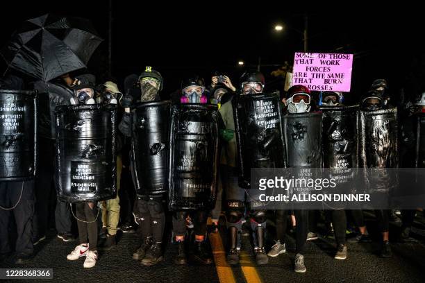 Protestors wearing gas masks and carrying homemade take part in the 100th day and night of protests against racism and police brutality in Portland,...