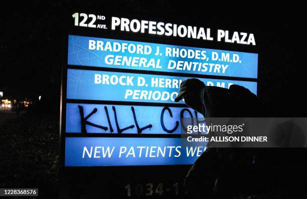 Protestor spray paints to write "Kill cops" on a business sign during the 100th day and night of protests against racism and police brutality in...