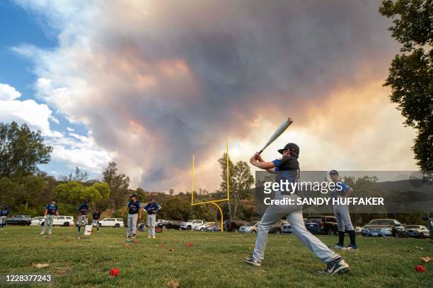 Little League players warm-up before a game as a brush fire is ablaze in back at a field next to the Sycuan Casino on the Sycuan Indian reservation...