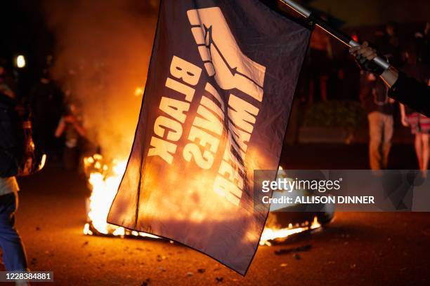 Black Lives Matter flag waves in front of a fire at the North Precinct Police building in Portland, Oregon on September 6, 2020. - Protestors are...