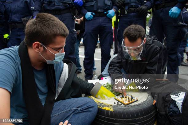 Climate activists, surrounded by police officers, hold onto a car tire filled with concrete while playing chess during a civil disobedience action on...