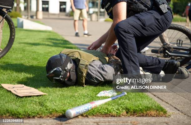 Black Lives Matter placard and a bat lie on the ground next to a member of the Proud Boys being arrested by Oregon police after allegedly attacking...