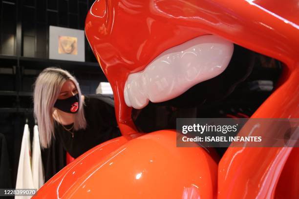An employee wearing a branded facemask poses looking at a giant "tongue and lip" logo inside The Rolling Stones new flagship store in London on...