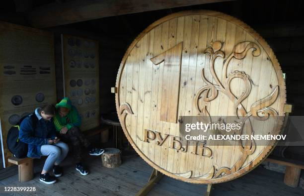 Couple sits next to a huge wooden Russian ruble coin in the center of the Siberian city of Tomsk on September 8, 2020. - The pandemic hit Russia...