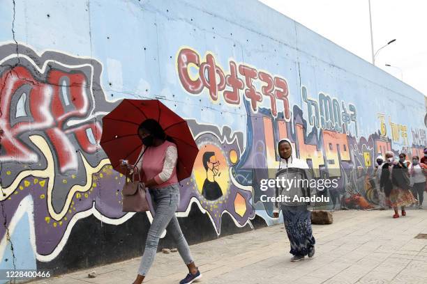 People walk past grafittis painted to raise the awareness of public on coronavirus on a wall in Addis Ababa, Ethiopia on September 08, 2020.