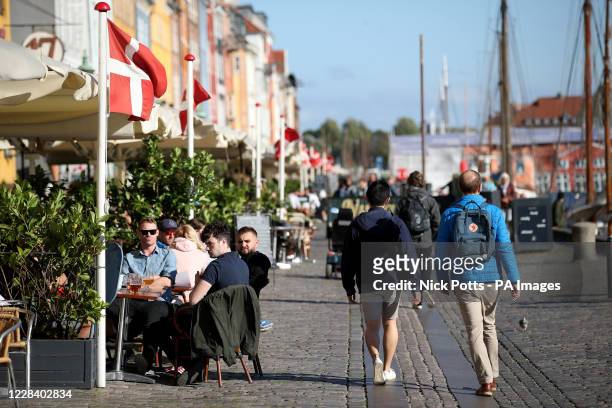 People sit and enjoy drinks in the sunshine at Nyhavn, a waterfront, canal and entertainment district in Copenhagen, Denmark