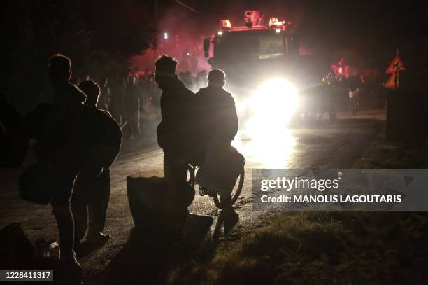 Migrants stand with their belongings after being evacuated as a fire burns in the Moria camp on the island of Lesbos on September 9, 2020. - The...