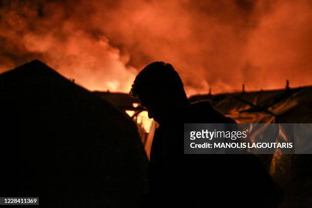 Migrant stands near tents as a fire burns in the Moria camp on the island of Lesbos on September 9, 2020. - The migrant camp of Moria, on the Greek...