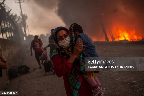 Woman carries a child past flames after a major fire broke out in the Moria migrants camp on the Greek Aegean island of Lesbos, on September 9, 2020....